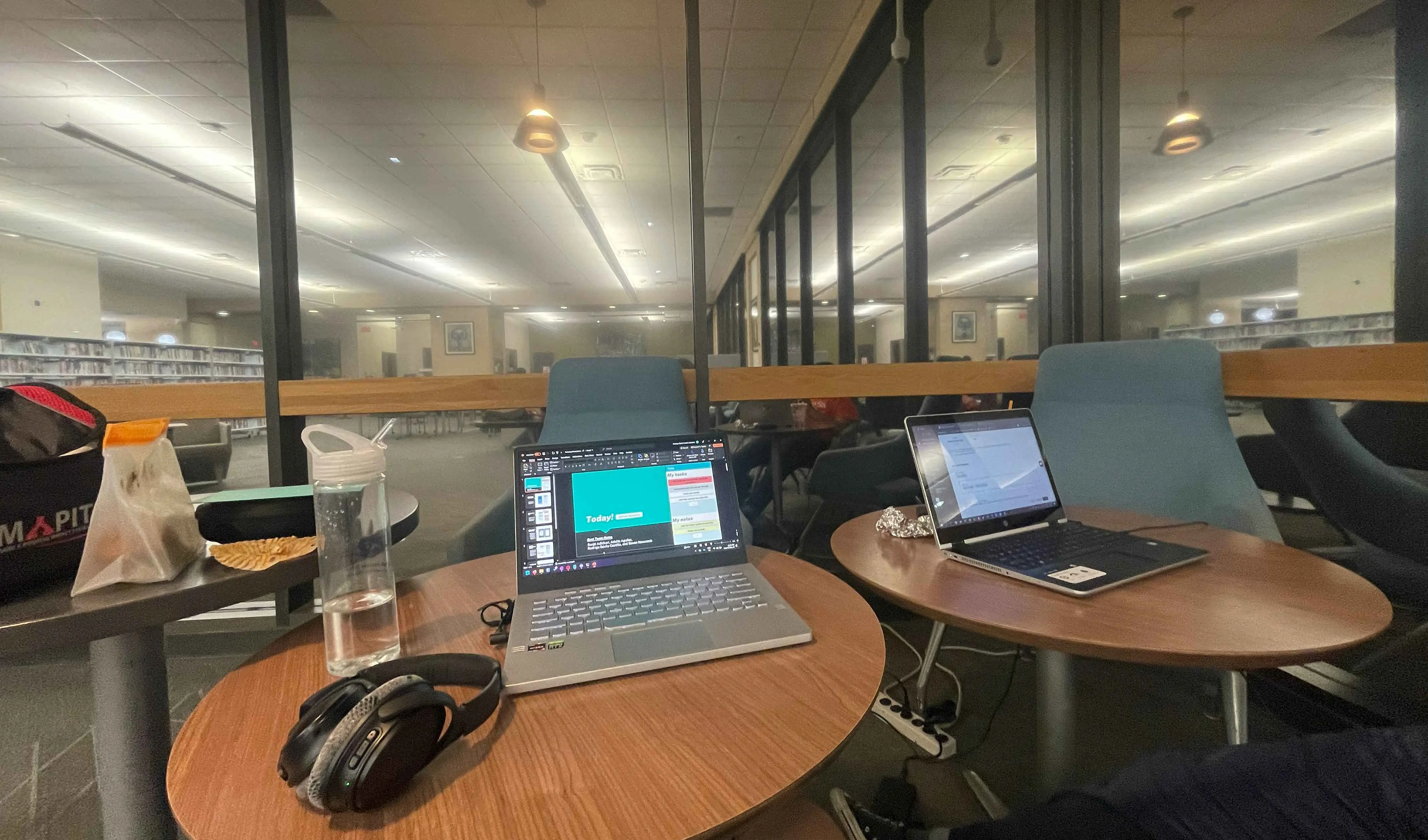 A nighttime picture of two laptops on library tables, with food wrappers scattered about the scene. The project PowerPoint is shown on the central laptop.